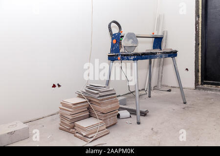 The professional tool of the builder a tile cutter and a stack of tiles in the bathroom, white plastered walls. Concept repair in apartments, laying o Stock Photo