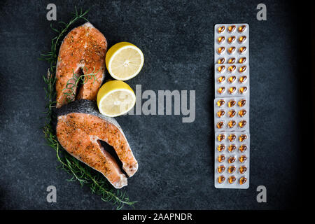 Fresh salmon steaks lie on a dark background, alongside lemon and rosemary, a peppercorn with various types of peppers and vitamins for daily consumpt Stock Photo