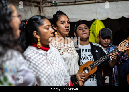 Zapateado dancers perform a traditional folk dance during a neighborhood Huapango in Santiago Tuxtla, Veracruz, Mexico. The dance involves dancers striking their shoes on a wooden platform while a large group of musicians play string instruments. The gatherings take part in the Los Tuxtlas mountain villages for single people to meet. Stock Photo