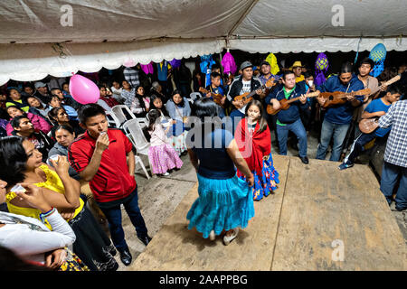 Zapateado dancers perform a traditional folk dance during a neighborhood Huapango in Santiago Tuxtla, Veracruz, Mexico. The dance involves dancers striking their shoes on a wooden platform while a large group of musicians play string instruments. The gatherings take part in the Los Tuxtlas mountain villages for single people to meet. Stock Photo