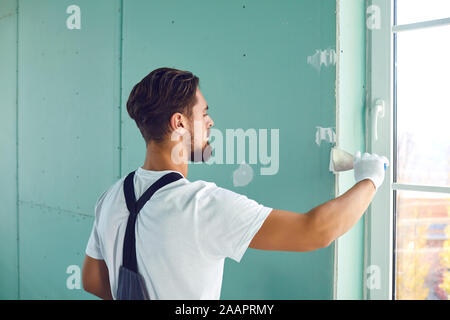 Worker builder plasterer plastering a wall of drywall at a construction site indoors Stock Photo