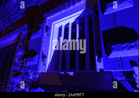 Old-fashioned window with strong metal bars at night, illuminated in blue Stock Photo