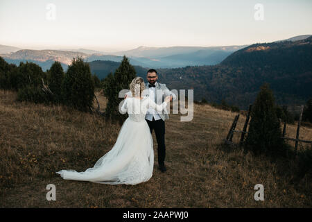 Beautiful couple having a romantic moment on their weeding day, in mountains at sunset. Dancing together. Stock Photo