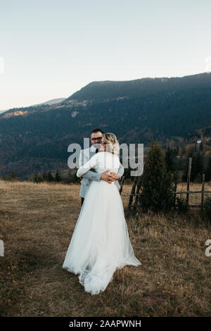Beautiful couple having a romantic moment on their weeding day, in mountains at sunset. Hugged couple. Stock Photo