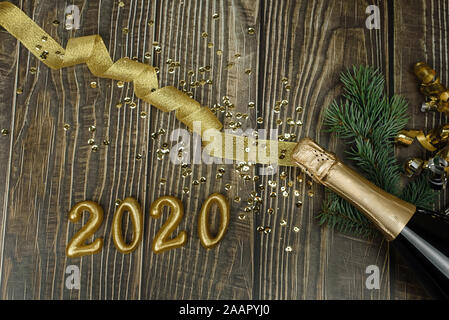 Champagne bottle with golden tinsel, ribbon and confetti on a dark wooden background. Golden bow, Christmas tree branch, bottle of champagne and numbe Stock Photo