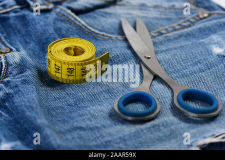 Tailors tools on denim fabric, selective focus. Making clothes and design concept. Jeans crotch and pocket, used as background. Metal scissors and yellow measure tape on jeans, close up. Stock Photo