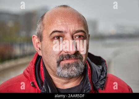 Close-up street portrait of an elderly balding man with a gray beard in warm clothes. The face of a middle-aged male older than 50 years outdoors. Fif Stock Photo