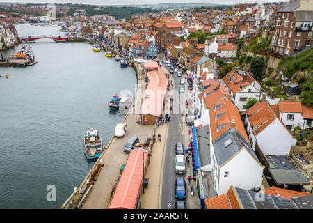 Cars and pedestrians alike travel past the docked boats in the seaside town of Whitby, Yorkshire, United Kingdom. Stock Photo