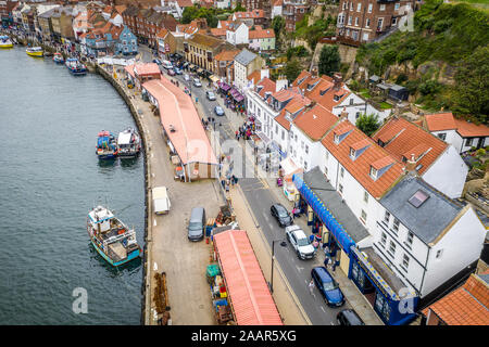 Cars and pedestrians alike travel past the docked boats in the seaside town of Whitby, Yorkshire, United Kingdom. Stock Photo