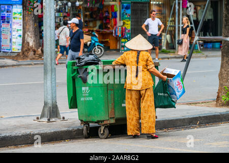 Hanoi, Vietnam - 12th October 2019: An Asian Woman carrys trash and rubbish out to the green waste bin in the streets of Hanoi, Vietnam, Asia Stock Photo