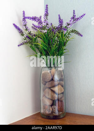Attractive and simple artificial flower arrangement of purple lavender flowers and pebbles in a glass vase. Stock Photo