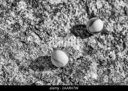 Black & white glass marbles on rough stone surface. For something lost, mental health, losing your marbles, abstract spheres, dreams, Biden & marbles. Stock Photo