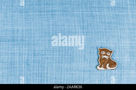 Cute gingerbread kitty-cat on blue textile background with grid texture. Sweet hand painted baked kitten on decorative fabric. Children's Day, cat day. Stock Photo