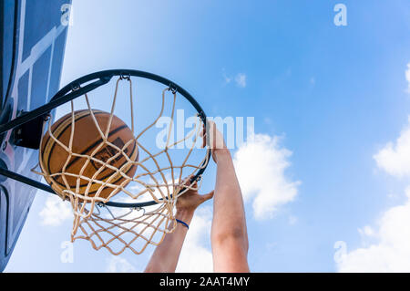 Young boy making a slam dunk in street basketball with blue sky and white clouds Stock Photo