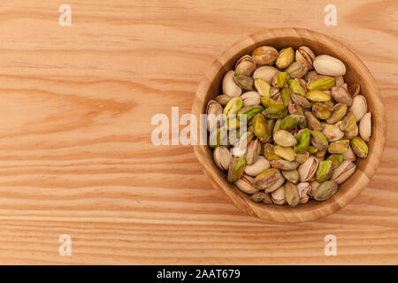 Top view of shell and peeled pistachios in wooden bowl and on wooden table. Stock Photo