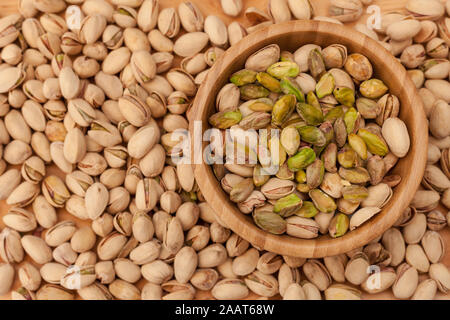 Top view of shell and peeled pistachios in wooden bowl and on wooden table. Stock Photo