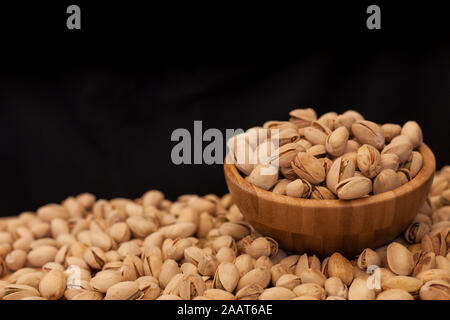 Shell pistachios in wooden bowl on wooden table and black background. Pistachios concept with copyspace. Stock Photo