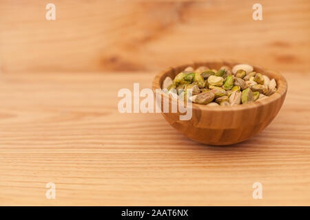 Shell and peeled pistachios in wooden bowl on wooden table. Pistachios concept with copyspace. Stock Photo