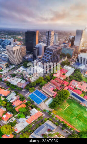 High-rise office towers in North Sydney CBD around historic post office building with school grounds of green lawn and sport courts - vertical aerial Stock Photo