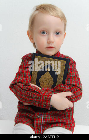 Little muslim European boy with islamic holy book Quran or Kuran Stock Photo