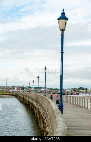 Mother and daughter walking dog along old English wooden jetty lined with street lamps Stock Photo