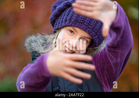 Smiling girl framing face with hands with blurry fall colours in the background Stock Photo