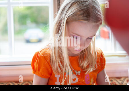 Little blonde girl dressed vibrantly in orange, looking down concentrating Stock Photo