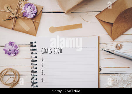 Top view of New Year Goals 2020 list empty note pad and christmas card on wooden table with xmas decoration. Stock Photo