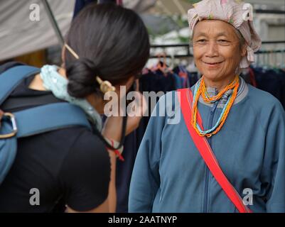 Japanese portrait photographer (tourist) takes a portrait photo of an elderly Thai Karen tribal woman with betel-nut stained lips at weekly market. Stock Photo