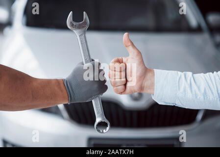 The auto mechanic holds the key in the client's hand and lifts his thumb up. Well done work Stock Photo