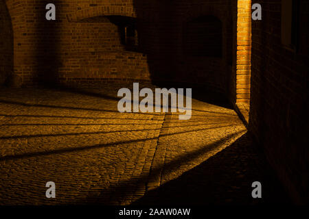 Light and shadow effect on cobblestone street at night, illumination from a niche in Barbican fortification in Old Town of Warsaw in Poland. Stock Photo