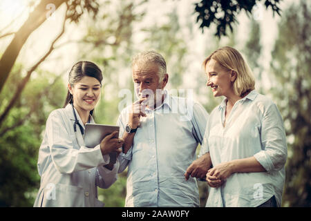 Senior couple man and woman talking to young nurse or caregiver in the park. Mature people healthcare and medical staff service concept. Stock Photo