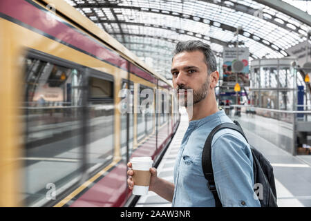 Man with takeaway coffee at the station while train coming in, Berlin, Germany