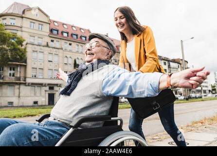 Laughing young woman pushing happy senior man in wheelchair Stock Photo