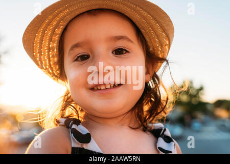 Portrait of smiling little girl wearing straw hat at sunset Stock Photo