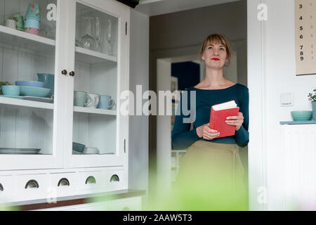 Portrait of woman with novel lening against door case at home Stock Photo