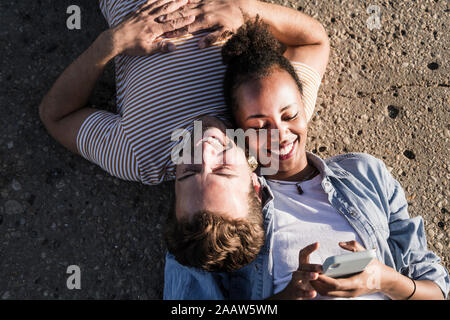 Happy young couple lying on concrete floor using cell phone Stock Photo
