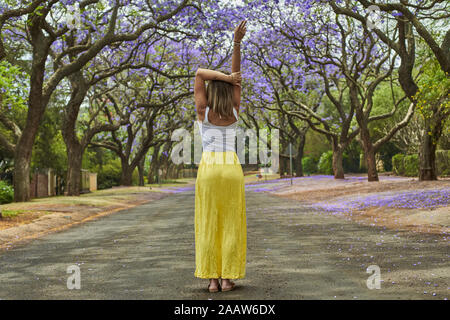 Woman in the middle of a street full of jacaranda trees in bloom, Pretoria, South Africa Stock Photo