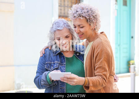 Senior mother with her adult daughter using smartphone outdoors