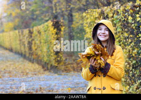 happy girl in a yellow hooded coat holds the leaves in her hands autumn season Stock Photo