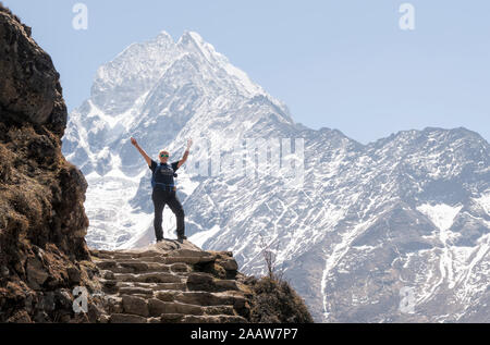 Happy woman raisng arms in front of Thamersku mountain, Himalayas, Solo Khumbu, Nepal Stock Photo