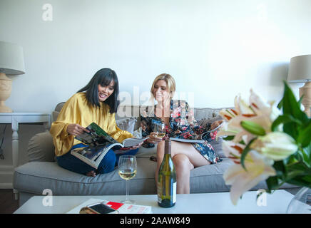 Friends sitting on couch, reading magazines, drinking wine Stock Photo