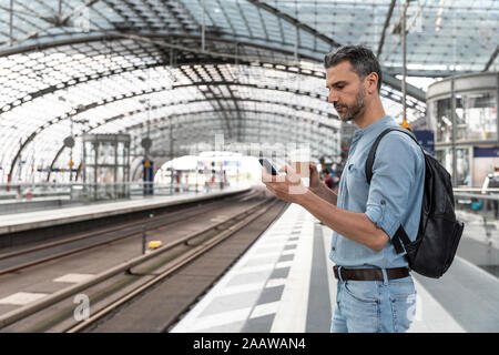 Businessman at the station waiting for the train looking at the smartphone, Berlin, Germany Stock Photo