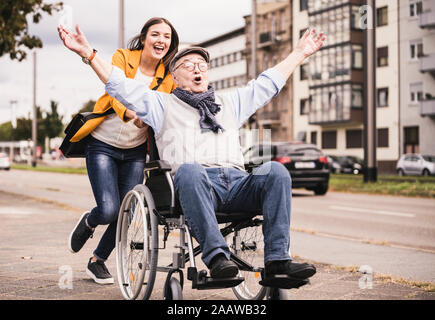 Portrait of young woman pushing senior man in wheelchair on pavement Stock Photo