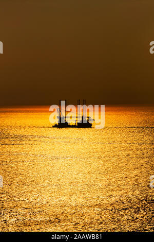 Offshore wind farm installation vessel sailing off in sea during sunset, West Coast, Scotland, UK Stock Photo