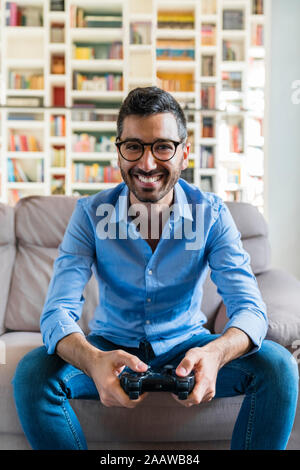 Portrait of laughing young man sitting on the couch at home playing video game Stock Photo