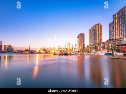 Illuminated buildings by river at Melbourne Docklands against blue sky at dusk, Victoria, Australia Stock Photo