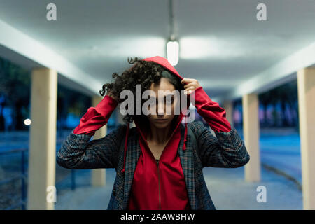 Portrait of young woman putting on hood in the evening Stock Photo