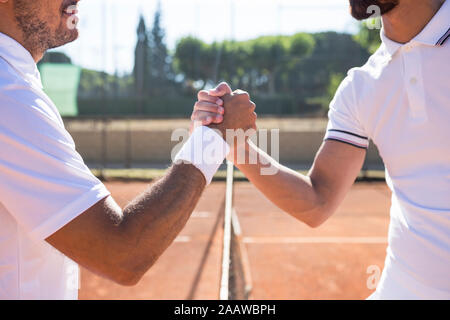 Side view of two tennis players with rackets shaking hands and smiling before tennis match Stock Photo