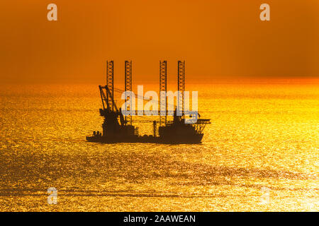 Silhouette offshore wind farm installation vessel sailing off in sea against sky during sunset, West Coast, Scotland, UK Stock Photo